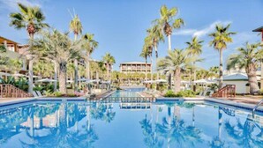 A large swimming pool surrounded by palm trees and a building with multiple balconies.