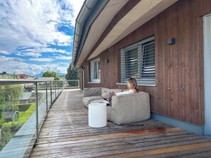 A modern house with a wooden deck, a grey sofa, and a white table.