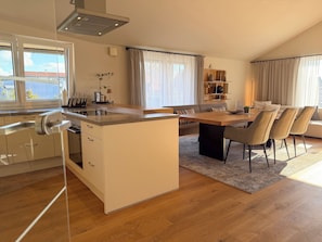 A modern kitchen with a central island, dining area with chairs, and a view of the outdoors. - Exclusive 4-room penthouse apartment "FIVE", near Salzburg (Seekirchen am Wallersee)