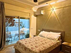 A hotel room with a bed, a nightstand, a wall-mounted air conditioner, and a sliding glass door leading to an outdoor area with a table and chairs. - 3-Bedroom Apartment with Panoramic Rooftop Terrace — Gauthier, Casablanca (Casablanca)
