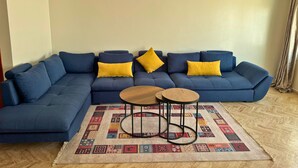 A living room with a blue sectional sofa, two wooden side tables, and a patterned rug.