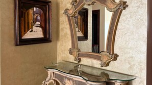 A room with a large ornate mirror, a framed painting, and an antique-style console table.