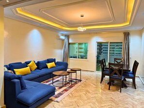 A living room with a blue sofa, a coffee table, and a dining area with chairs and a table. - 3-Bedroom Apartment with Panoramic Rooftop Terrace — Gauthier, Casablanca (Casablanca)