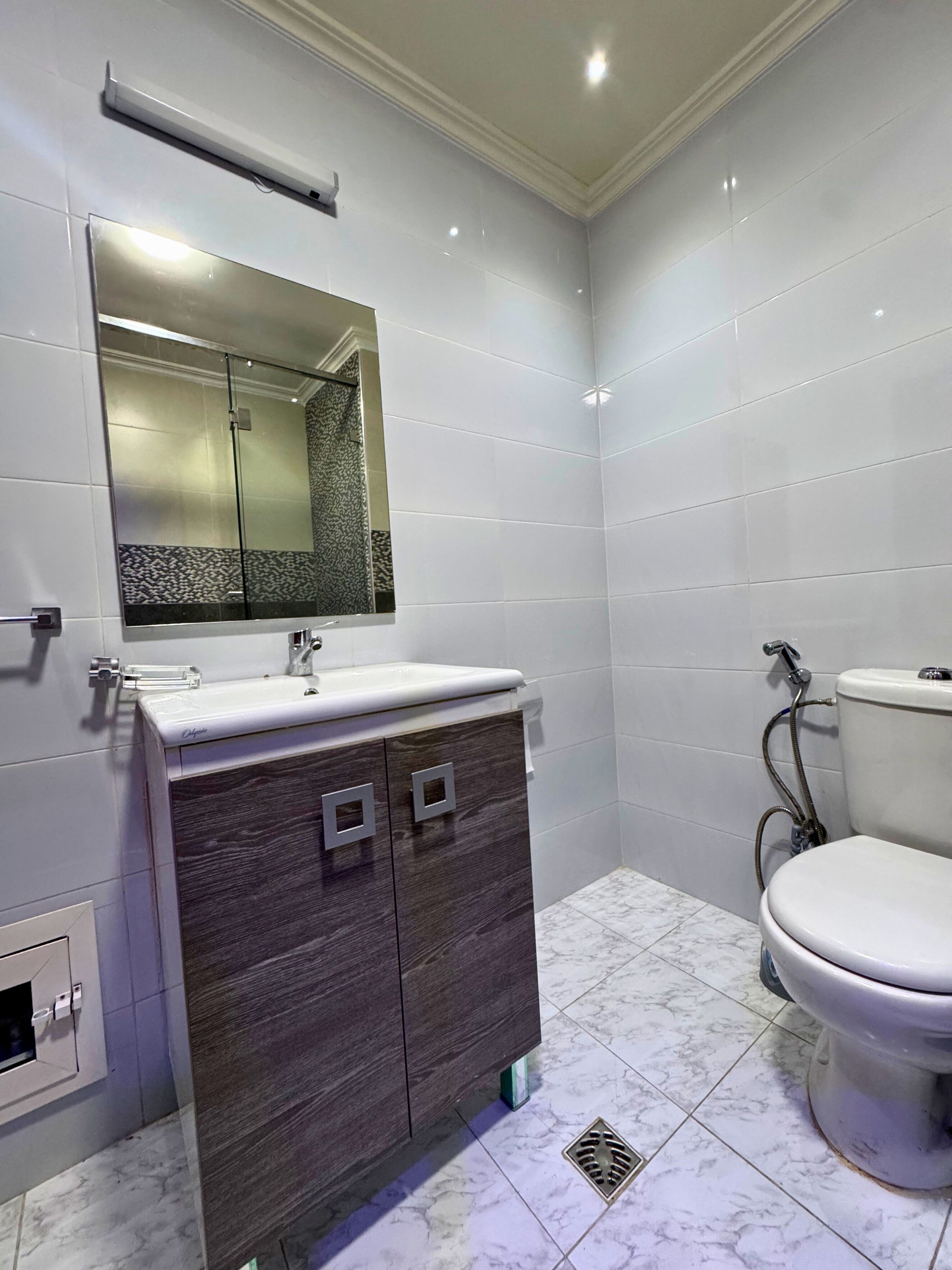 A modern bathroom with a vanity, mirror, toilet, and tiled walls.