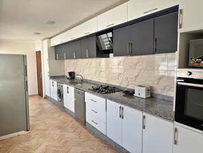 A modern kitchen with a stainless steel refrigerator, a washing machine, a dishwasher, a gas stove, and a microwave.