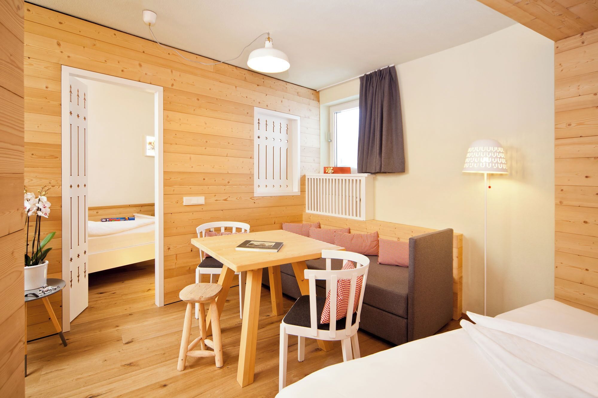 Ein gemütliches Zimmer mit Holzboden, einem Bett, einem Tisch mit Stühlen, einer Couch und einer Lampe.