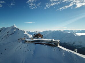 A snow-covered mountain lodge with a ski lift, surrounded by snow-covered peaks and clear skies. - Glacier Hotel Grawand (Senales)