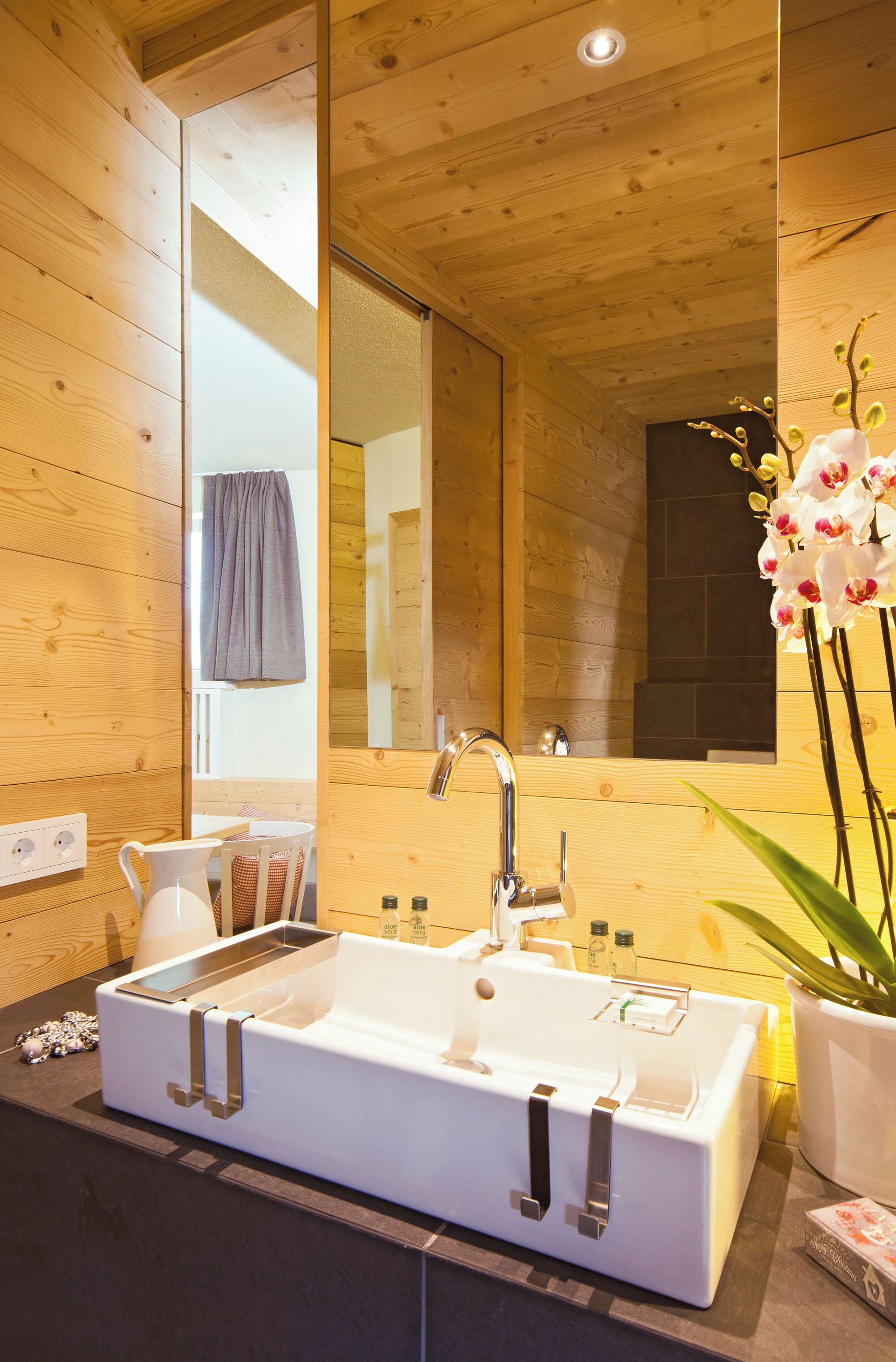 A modern bathroom with a large mirror, a white sink, and a potted orchid.