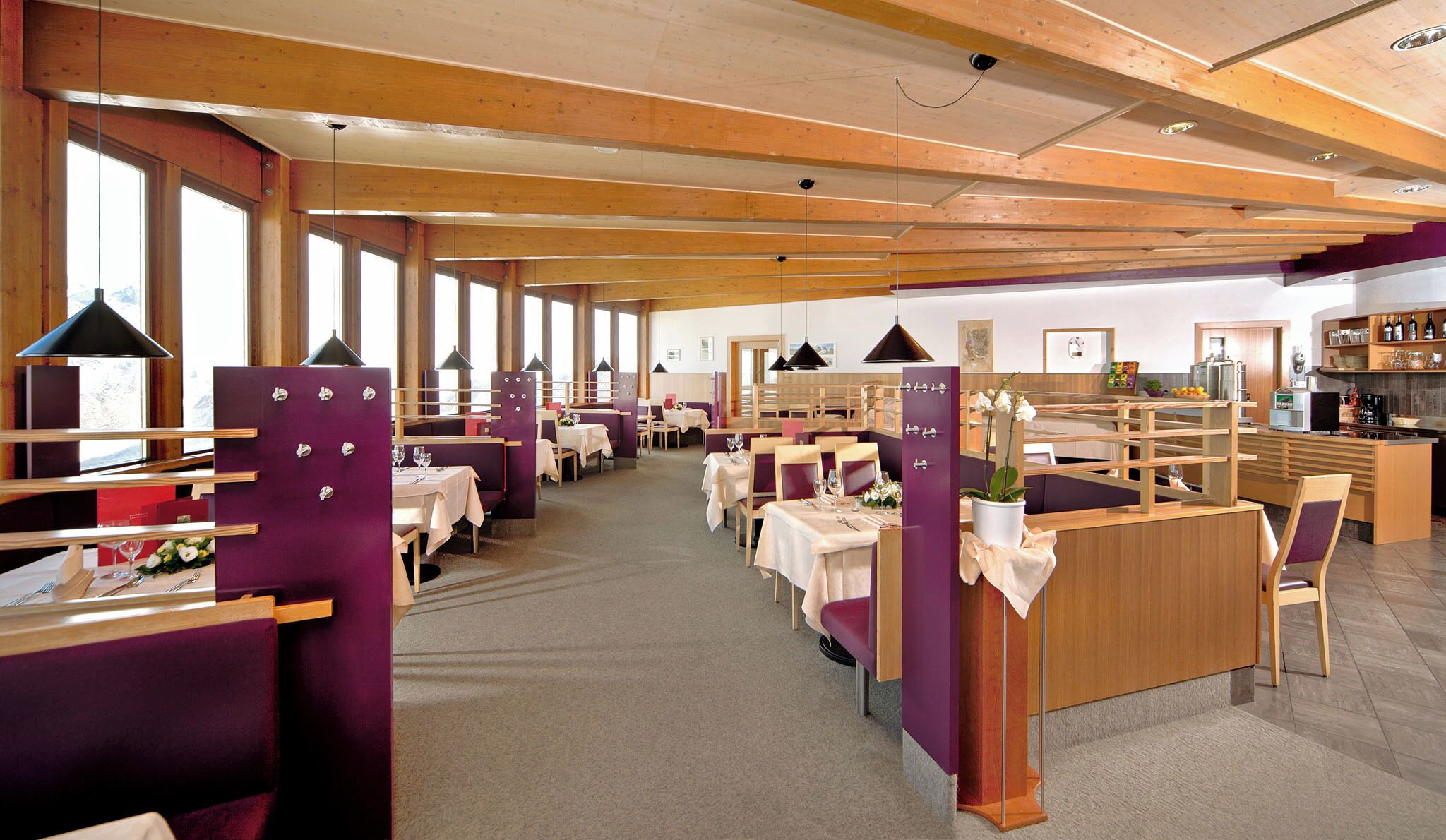 A restaurant with wooden beams, purple booths, and tables set for dining.