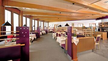 A restaurant with wooden beams, purple booths, and tables set for dining.