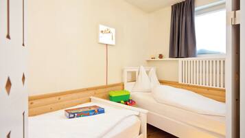 Una habitación infantil con literas, una mesita de noche pequeña, un baúl de juguetes y una ventana con cortinas.