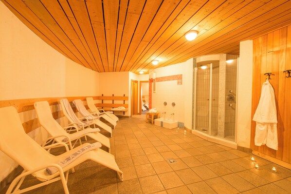 A sauna room with wooden benches, a glass-enclosed shower, and a white towel hanging on a hook. - Glacier Hotel Grawand (Senales)