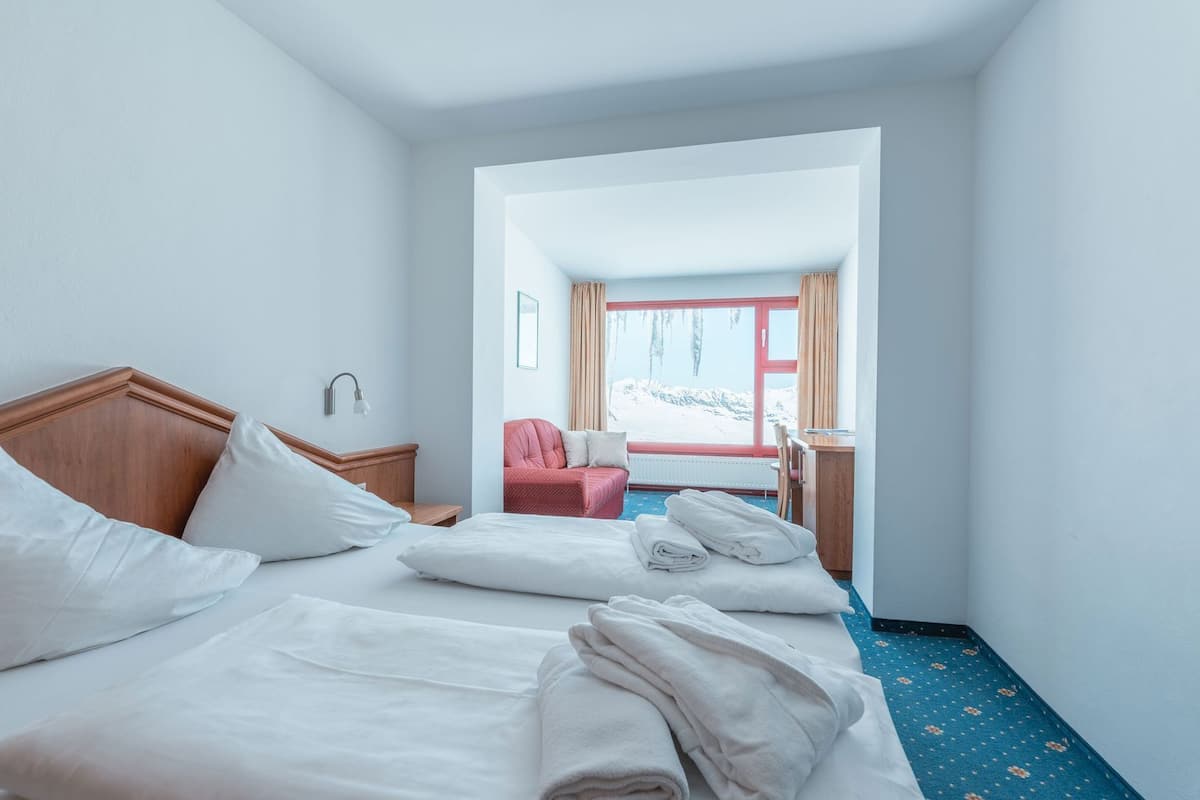 A hotel room with two beds, a wooden headboard, a desk, a chair, and a view of a snowy landscape through a window.