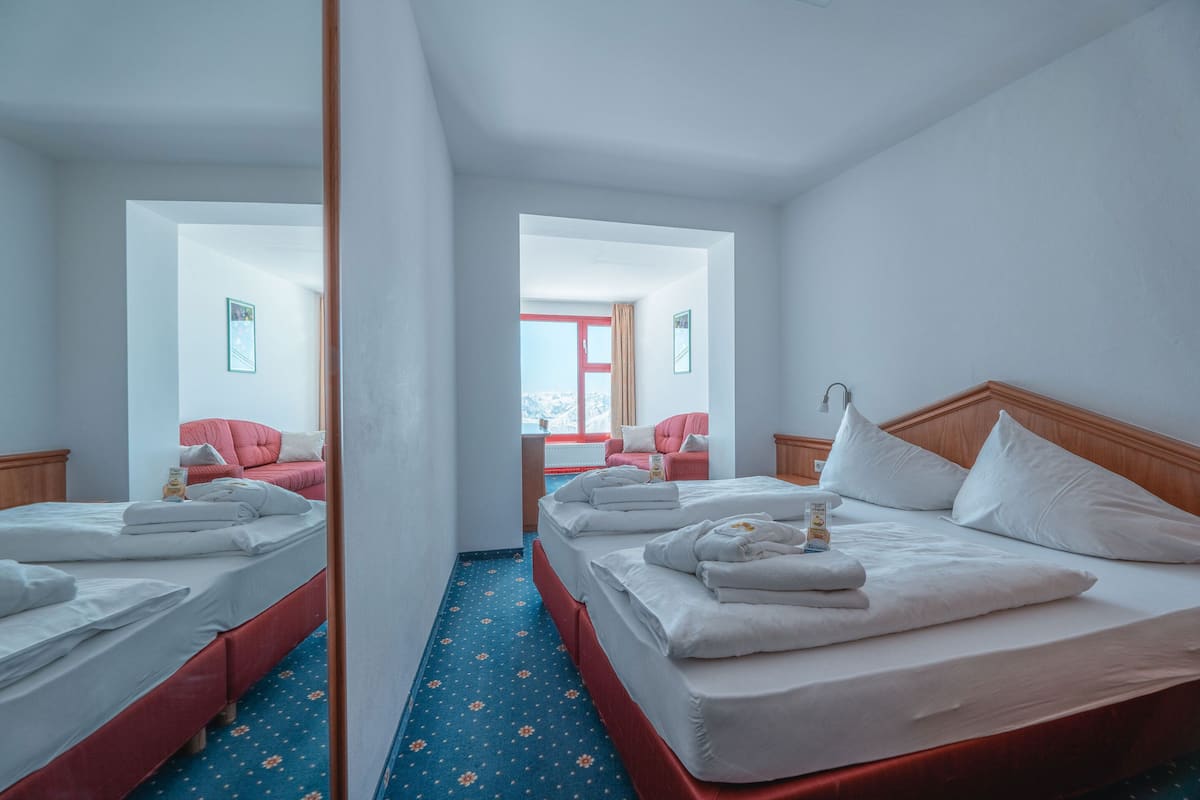 A hotel room with two beds, a red sofa, a wooden headboard, and a blue carpet with a floral pattern.