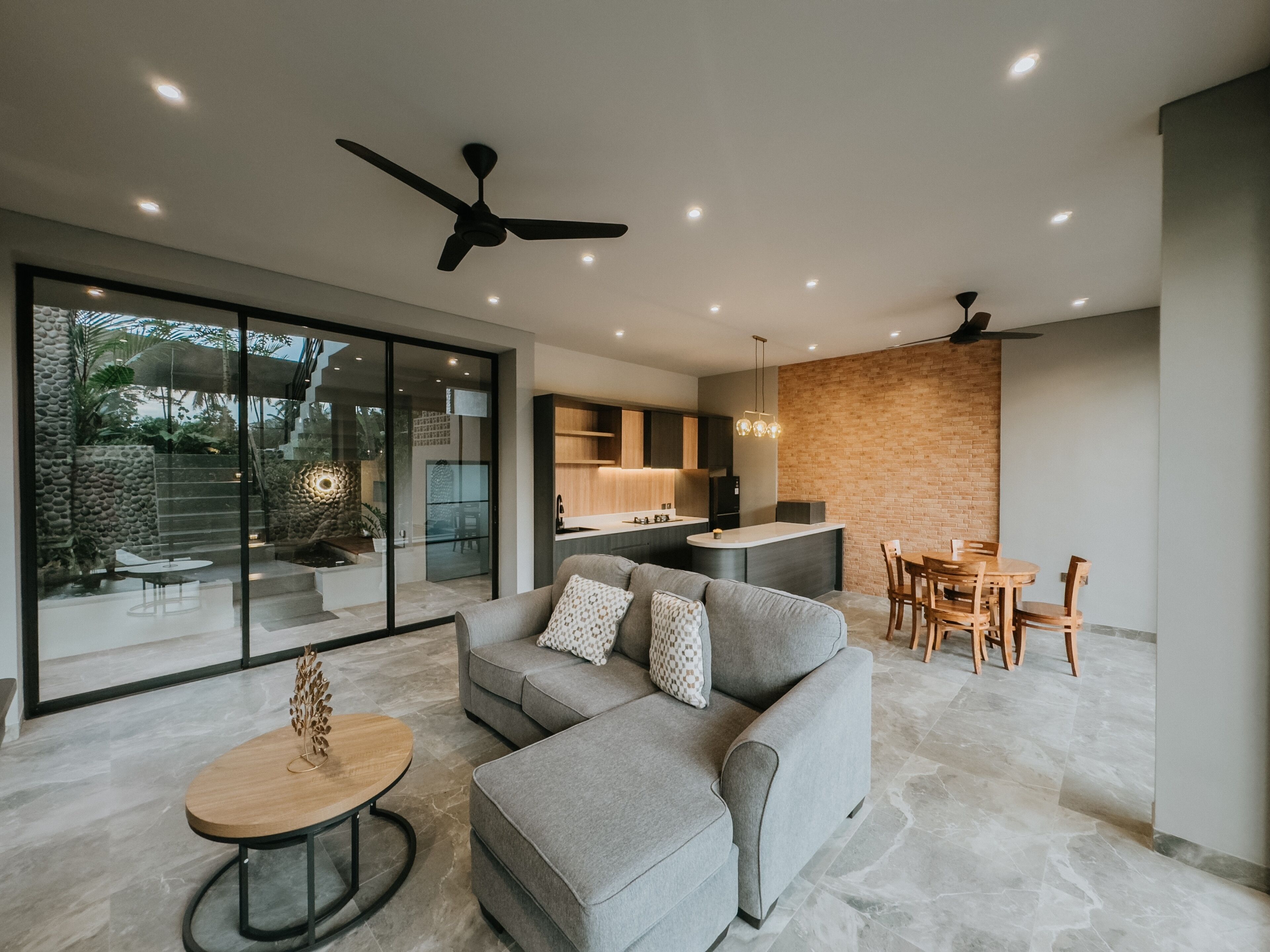 A modern living room with a grey sofa, a wooden coffee table, and a dining area with wooden chairs.
