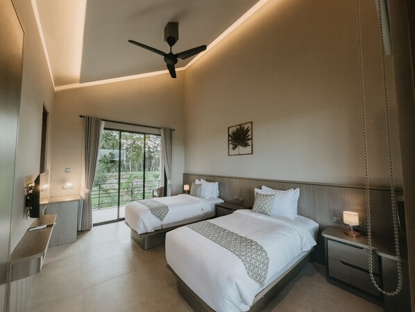 A hotel room with two beds, a ceiling fan, a large window with curtains, a small table with a lamp, and a wall-mounted artwork.