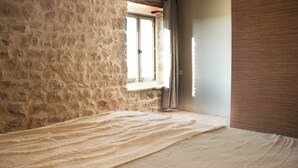 Een kamer met een stenen muur, een raam en een bed met een witte deken.