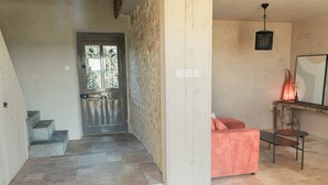 Een modern interieur met een stenen muur, een houten deur met glaspanelen, een trap, een roze bank, een kleine tafel en een hanglamp.
