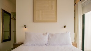 A neatly made bed with white linens, a framed abstract artwork above it, and a nightstand with a lamp to the left. - w Stunning 1BR in Miraflores (Lima)
