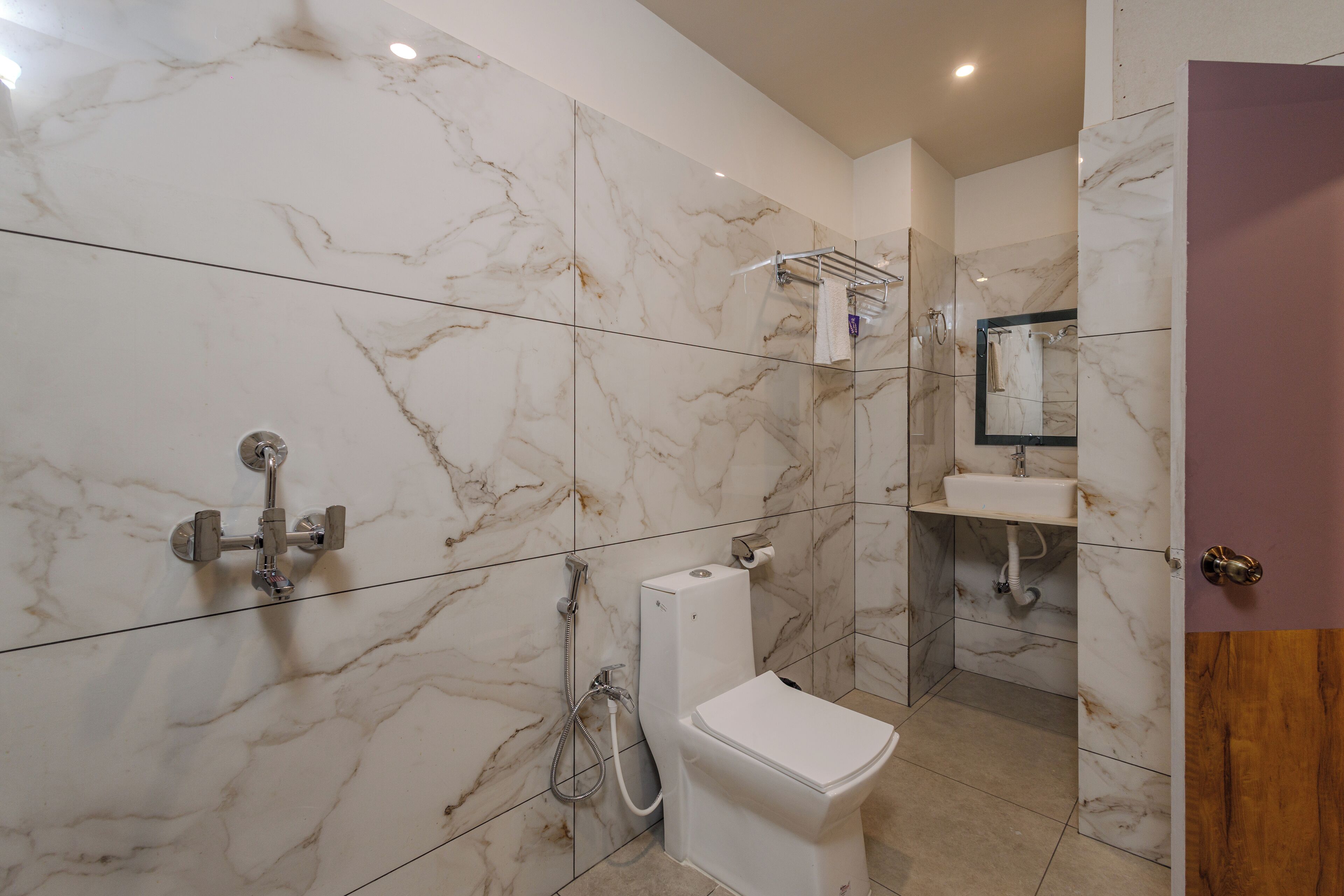 A bathroom with a toilet, sink, and shower area, all with marble walls and a modern design.