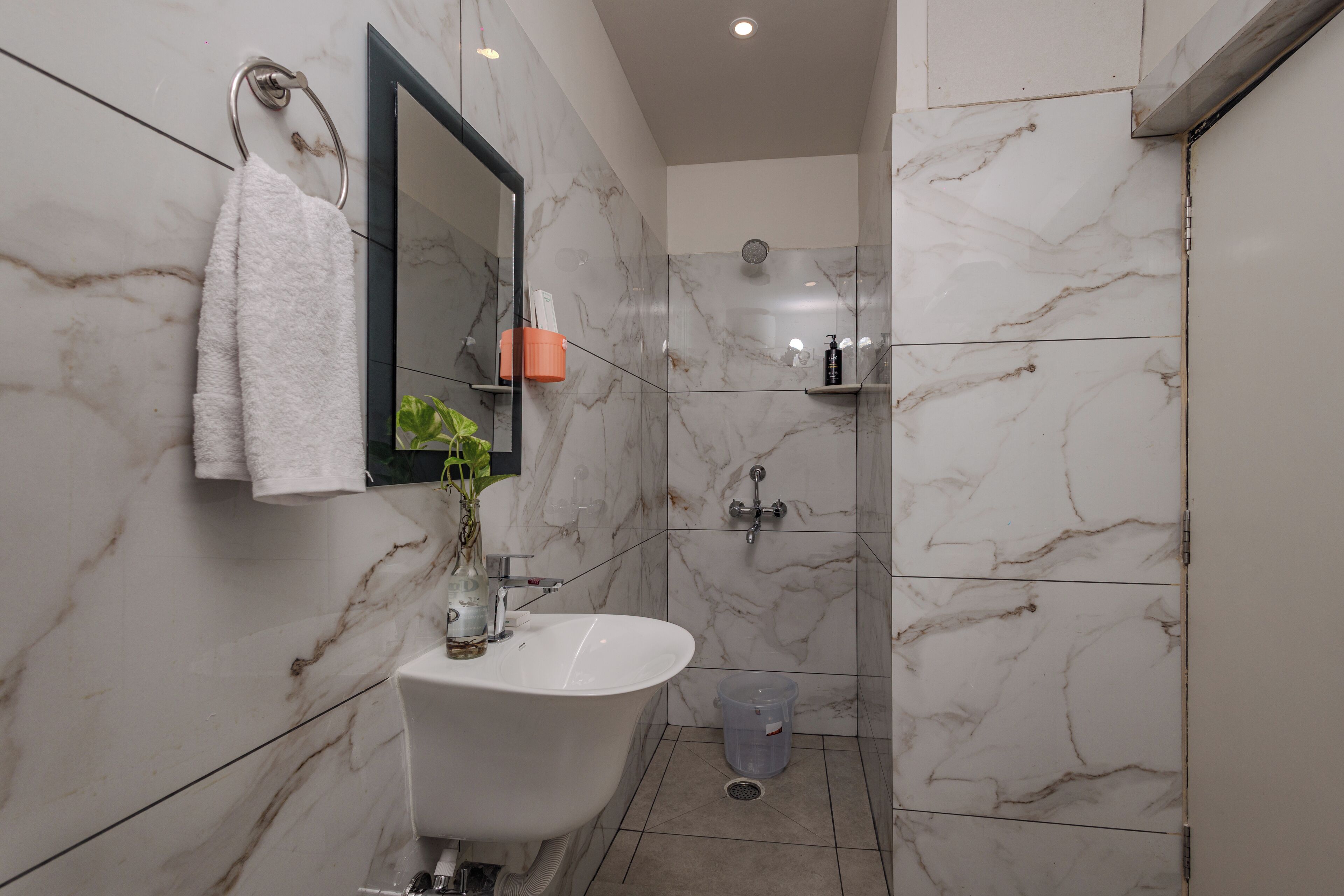Un baño con lavamanos blanco, espejo, toallero, zona de ducha y pared de mármol.