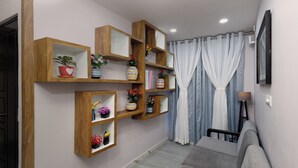 A living room with a grey sofa, wooden shelves with decorative items, a grey curtain, and a wall-mounted TV. - Bestaay- A Boutique Hotel (Near INFOCITY and KIIT) (Bhubaneshwar)