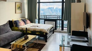 A modern hotel room with a bed, a sofa, a glass table, a TV, and a city view. - Makati City Poblacion (Makati)
