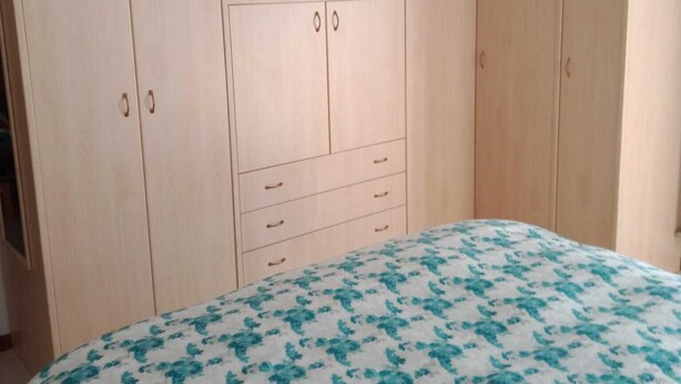 Un dormitorio con una cama, un televisor montado en un mueble de madera y una lámpara en el techo.