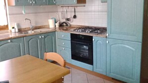 Una cocina con armarios verde azulado, una mesa de comedor de madera y una estufa negra.