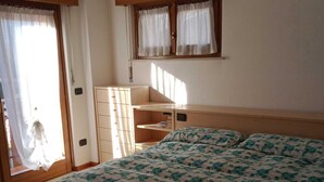 Un dormitorio con cama, cómoda, ventana con cortinas y luz en el techo.