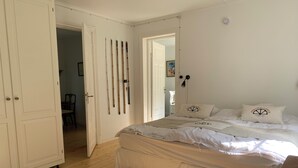 A bedroom with a bed, wooden floor, white walls, and a door leading to another room.