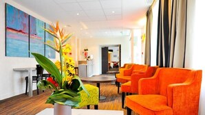 A modern hotel lobby with bright orange seating, a central round table, and a large plant. - Hôtel le saint pierre  (Mézidon Vallée d'Auge)