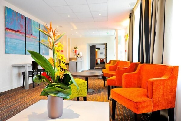 Eine moderne Hotelhalle mit leuchtend orangefarbenen Sitzgelegenheiten, einem runden Tisch in der Mitte und einer großen Pflanze.
