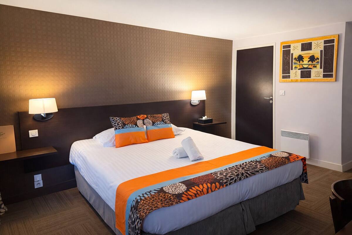A hotel room with a large bed, two bedside lamps, a wall-mounted artwork, and a visible door.