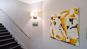 A staircase with a metal handrail, a wall-mounted light fixture, and a large abstract painting. - Hôtel le saint pierre  (Mézidon Vallée d'Auge)