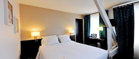 A hotel room with a large bed, two bedside lamps, a desk with a chair, and a window with curtains.