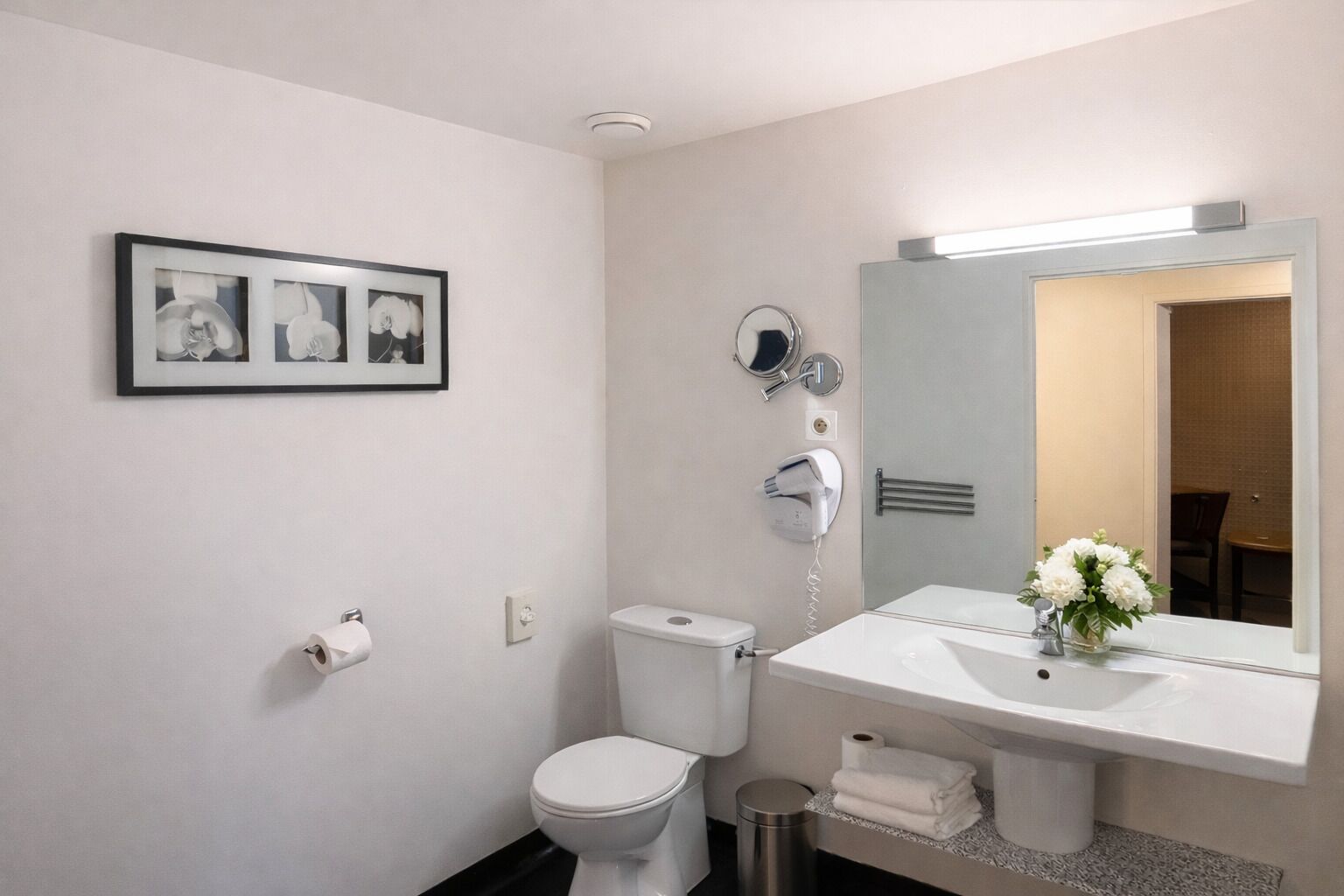 A bathroom with a toilet, sink, mirror, and framed pictures on the wall.