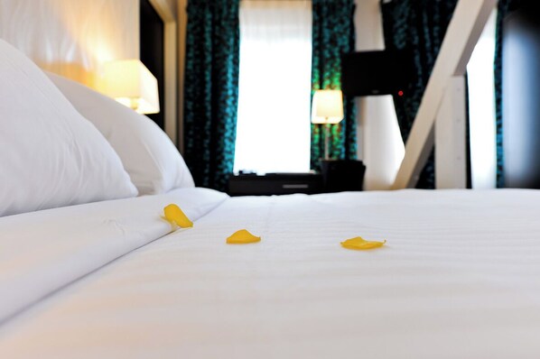 A hotel room with a neatly made bed, a television on the wall, and a window with curtains.