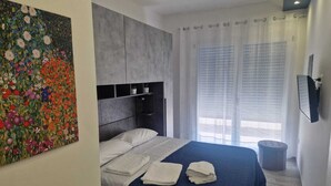 A hotel room with a bed, a headboard, a painting, a window with blinds, and a television on the wall. - KLIMT HOUSE. (Marsala)