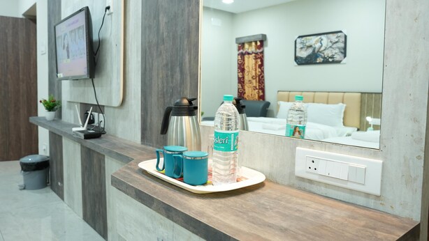 A hotel reception area with a wooden counter, a coffee machine, two blue mugs, and a water bottle. - RMV Inn (Katpadi)