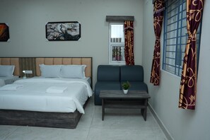 A modern bedroom with a large bed, a sofa, a small table with a plant, and a window with curtains.