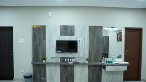 A reception area with a flat-screen TV mounted on a marble wall, a counter with a sink, and a trash bin. - RMV Inn (Katpadi)