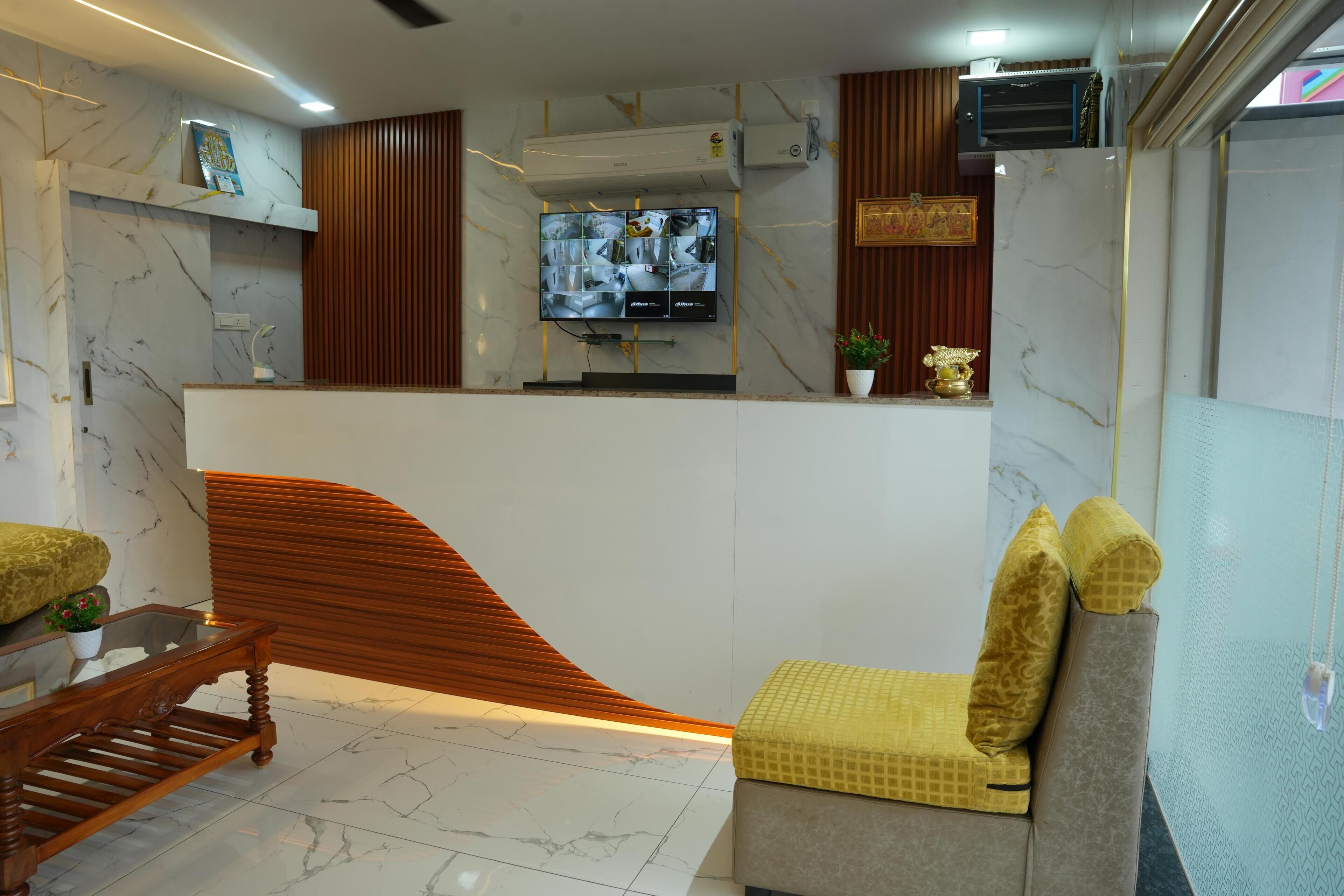 A modern reception area with a marble wall, a wooden reception desk, a flat-screen TV, and a seating area with cushions.