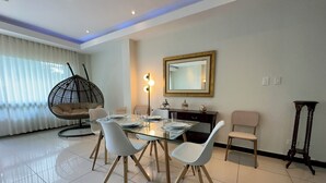 A modern dining area with a glass table, white chairs, a hanging chair, and a dark wooden cabinet. - Exceptional three-bedroom, two-and-a-half-bathroom ground floor condo (Playa Hermosa)