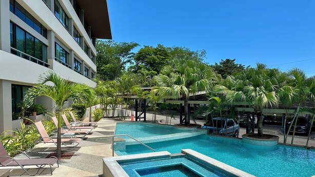 A swimming pool area with lounge chairs and palm trees. - Exceptional three-bedroom, two-and-a-half-bathroom ground floor condo (Playa Hermosa)