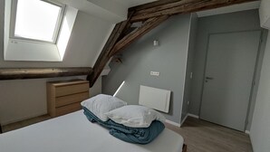 Une chambre avec un plafond en pente, une fenêtre, une table de chevet, un lit avec des oreillers, une armoire et une porte.