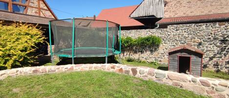 A stone house with a red-tiled roof, a trampoline with a safety net, and a small wooden shed.