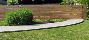A wooden fence with a small bush in front, a concrete pathway, and a grassy area.