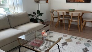 A living room with a sofa, a coffee table, a dining table with chairs, a large mirror, and a painting on the wall. - Bright apartment with terrace Private parking (Rouen)