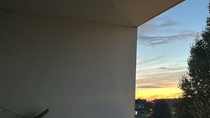 A balcony with a view of a sunset, a table with a glass, and a chair. - Bright apartment with terrace Private parking (Rouen)